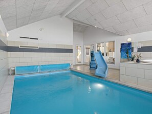 An indoor swimming pool with a blue slide, a reception desk, and a view into the adjacent room. - 5 Star Holiday Home in Bogense (Bogense)
