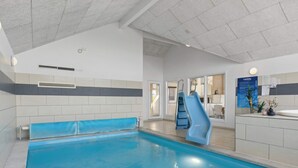 En inomhuspool med en blå vattenrutschkana, en reception och en synlig trappa som leder till ett annat rum.