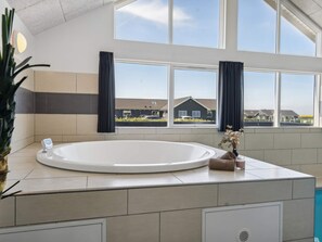 A modern bathroom with a large bathtub, a window, and a view of houses. - 5 Star Holiday Home in Bogense (Bogense)