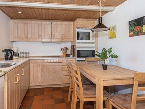 A kitchen with wooden cabinets, a stove, a microwave, and a dining table with chairs. - 3 Person Holiday Home in Høll Børkop (Borkop)