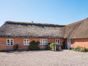 A thatched-roof building with a gravel driveway and a small garden area.