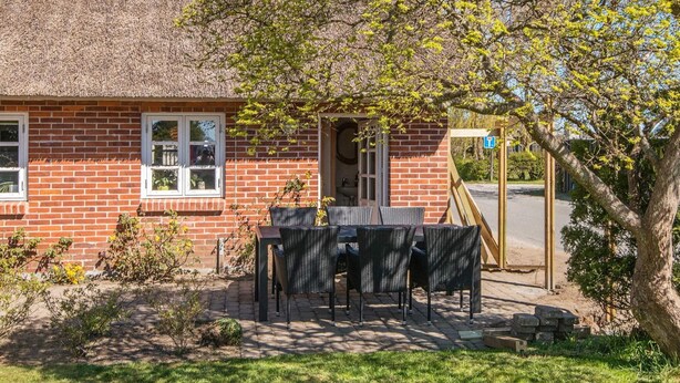 A brick house with a thatched roof, a patio with outdoor furniture, and a tree in the foreground. - 3 Person Holiday Home in Høll Børkop (Borkop)