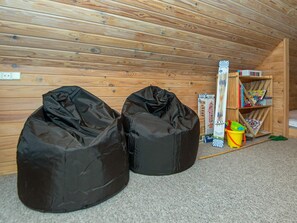 A room with a sloped ceiling, wooden walls, and a carpeted floor. There are two black bean bags and a small bookshelf with children's books and toys.
