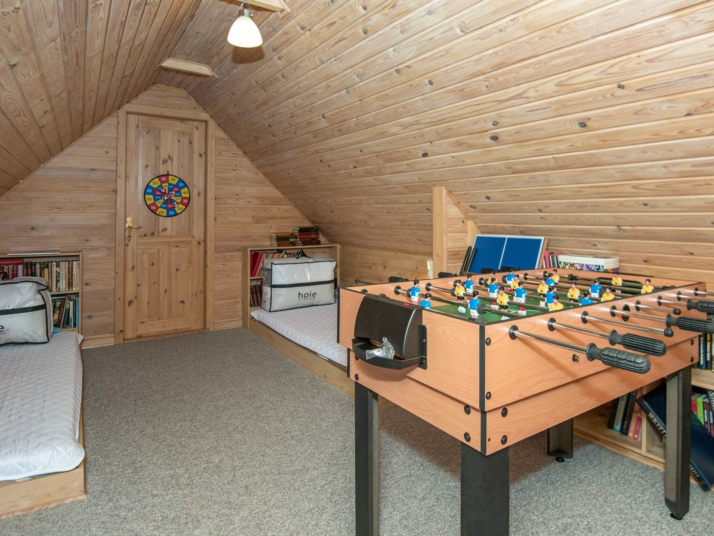 Un acogedor dormitorio en el ático con mesa de fútbol, cama, dardo y estantería.