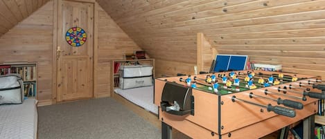 Une pièce mansardée chaleureuse, équipée d’un baby-foot, d’un lit, d’une cible de fléchettes et d’une bibliothèque.