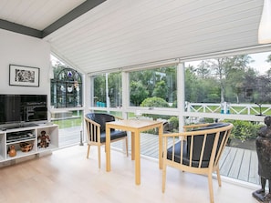 A sunroom with a TV, wooden furniture, and large windows overlooking a garden. - Elegant Holiday Home in Jerup near Sea (Jerup)