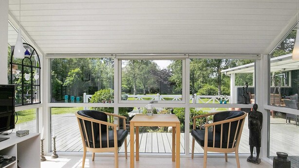 A conservatory with a wooden table and two chairs, large windows, and a view of a garden. - Elegant Holiday Home in Jerup near Sea (Jerup)