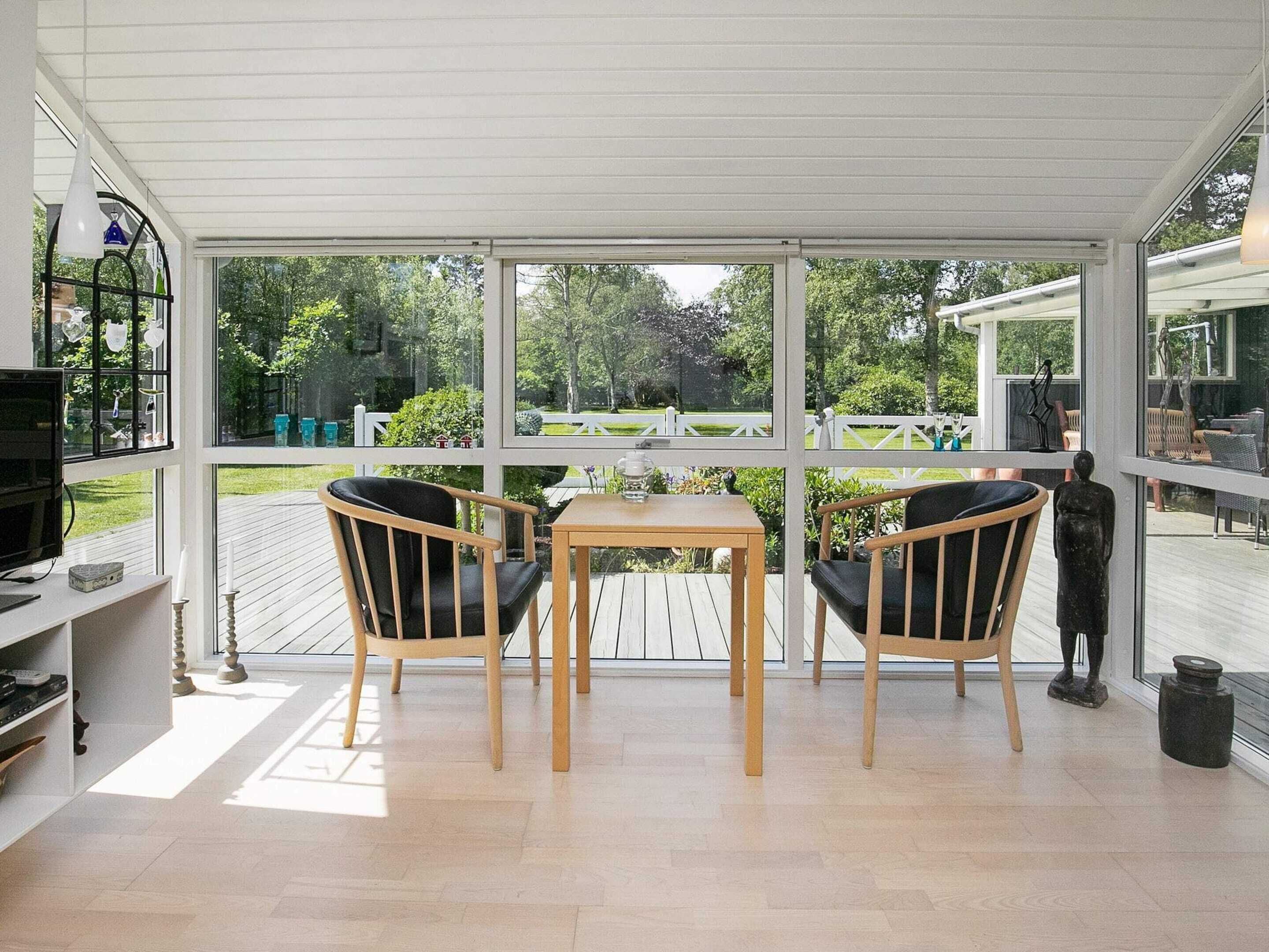 A conservatory with a wooden table and two chairs, large windows, and a view of a garden. - Elegant Holiday Home in Jerup near Sea (Jerup)