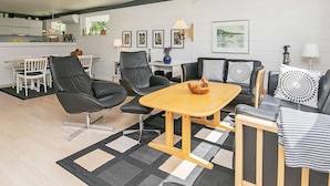 A modern living room with a dining area, featuring a wooden coffee table, black leather chairs, and a black and white patterned throw pillow. - Elegant Holiday Home in Jerup near Sea (Jerup)