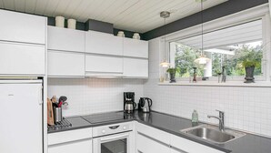 A modern kitchen with white cabinetry, a black countertop, a built-in oven, a coffee maker, and a window with plants. - Elegant Holiday Home in Jerup near Sea (Jerup)