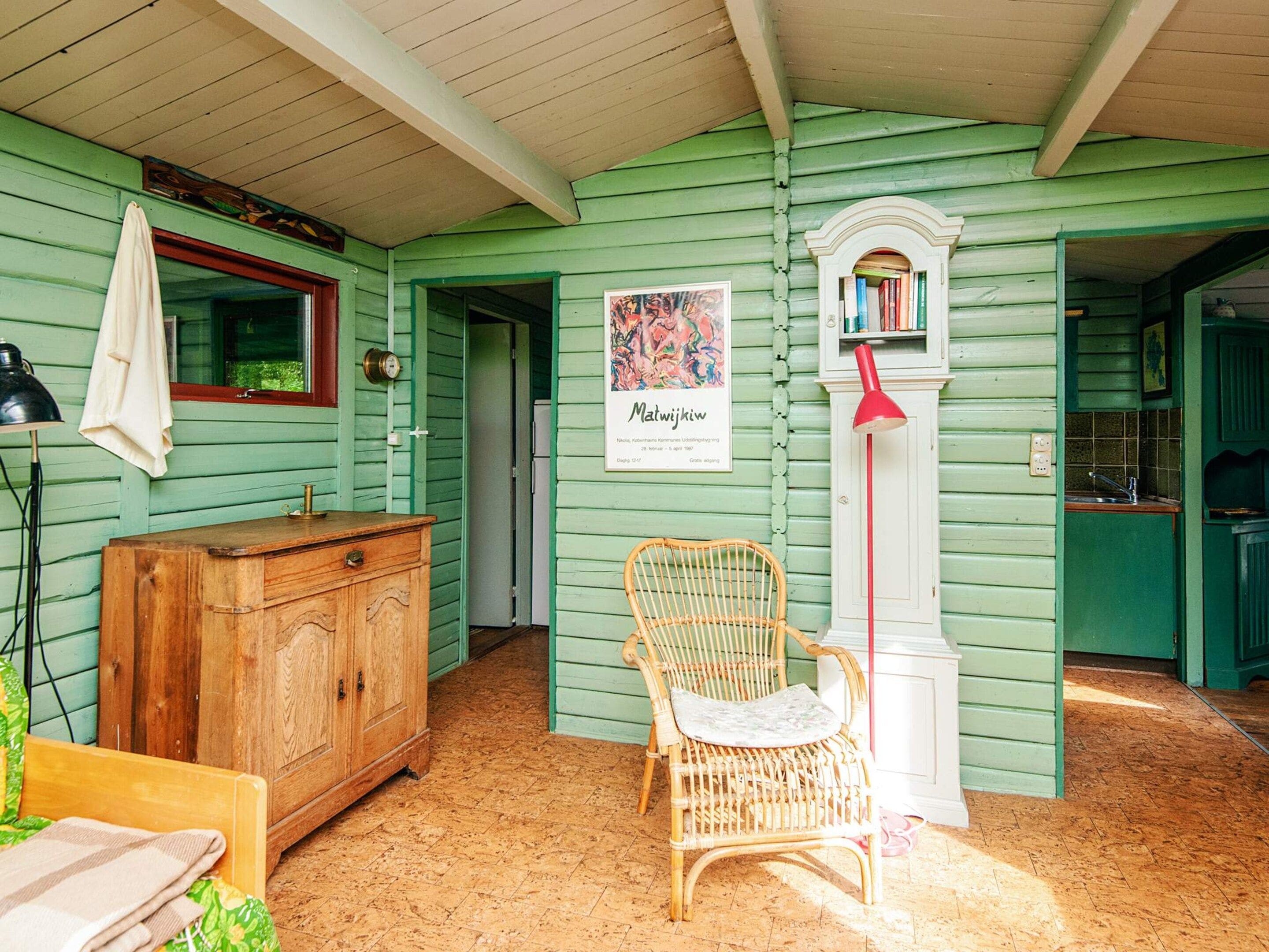 A room with green walls, a wooden cabinet, a wicker chair, a red lamp, and a framed picture on the wall.