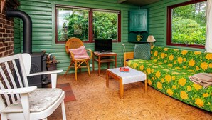 Una habitación acogedora con una pared verde, un sofá de madera con estampado floral, una silla de mimbre, una mesita pequeña y un televisor.