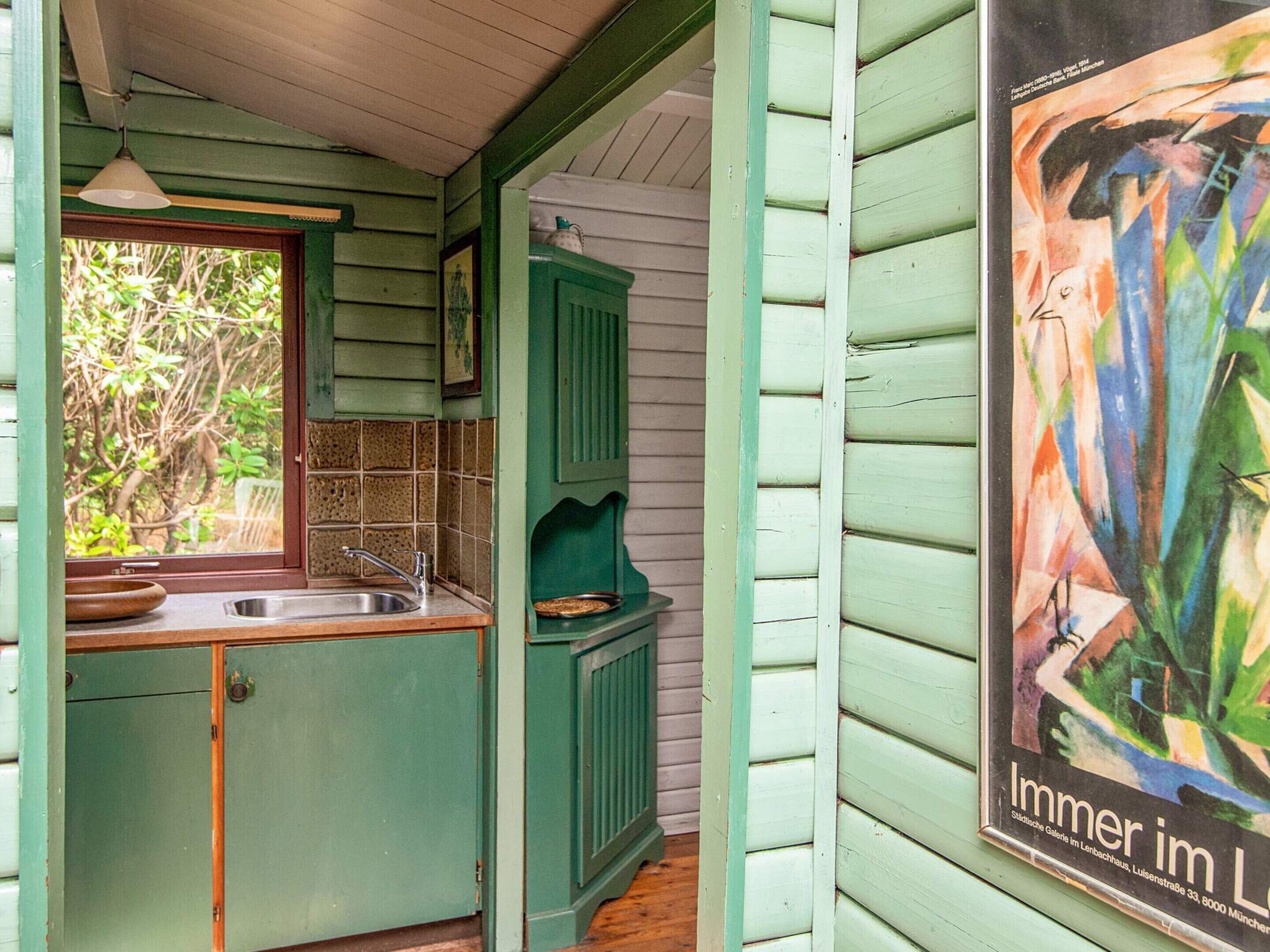 Una cocina con ventana, un lavamanos y un armario verde.