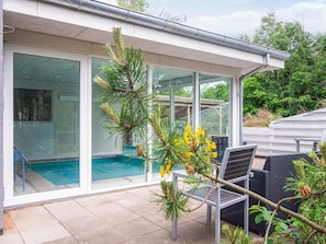 A modern house with a glass-enclosed pool, outdoor seating, and a view of the surrounding greenery.