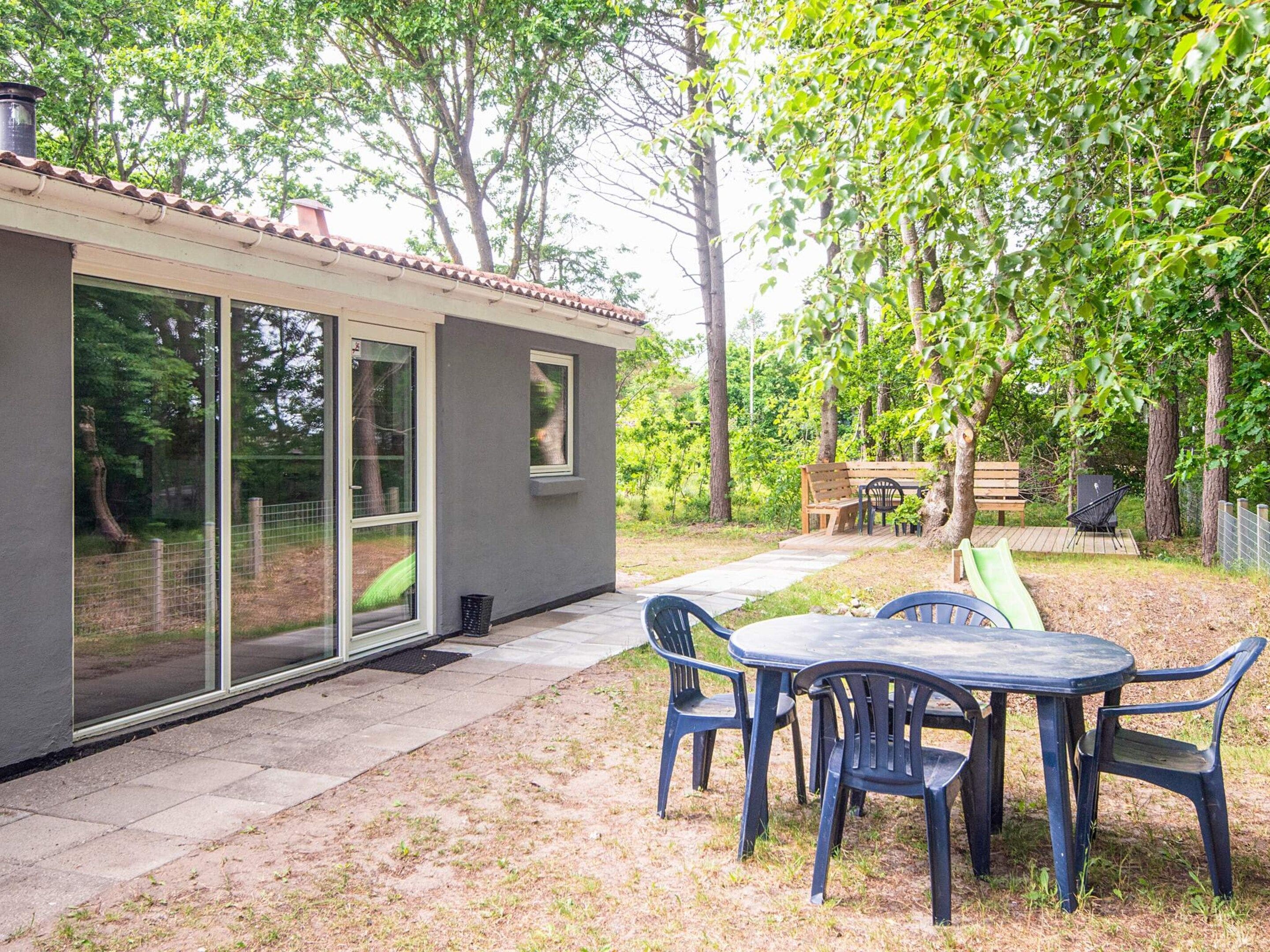 A modern house with a patio, a table with chairs, and a wooden deck.