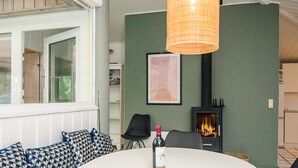 A cozy living room with a white sofa, a table with a magazine, a bottle of wine, and a fireplace. - 7 Person Holiday Home in Orsted (Ørsted)