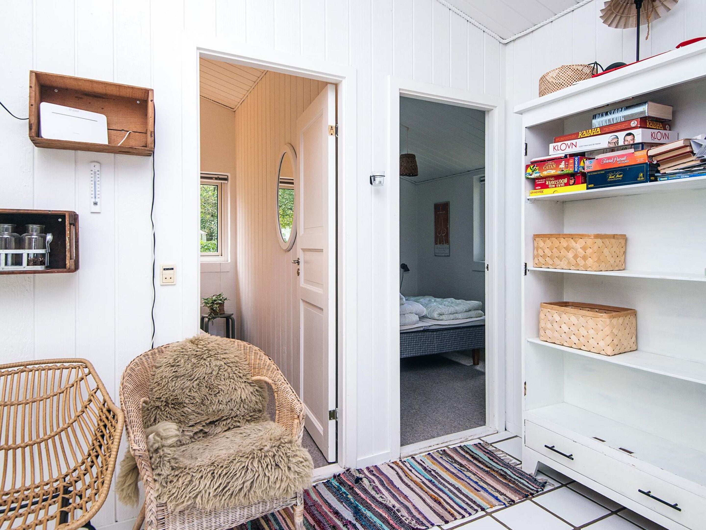 A room with a bed, a chair, a shelf with books, and a door leading to another room.