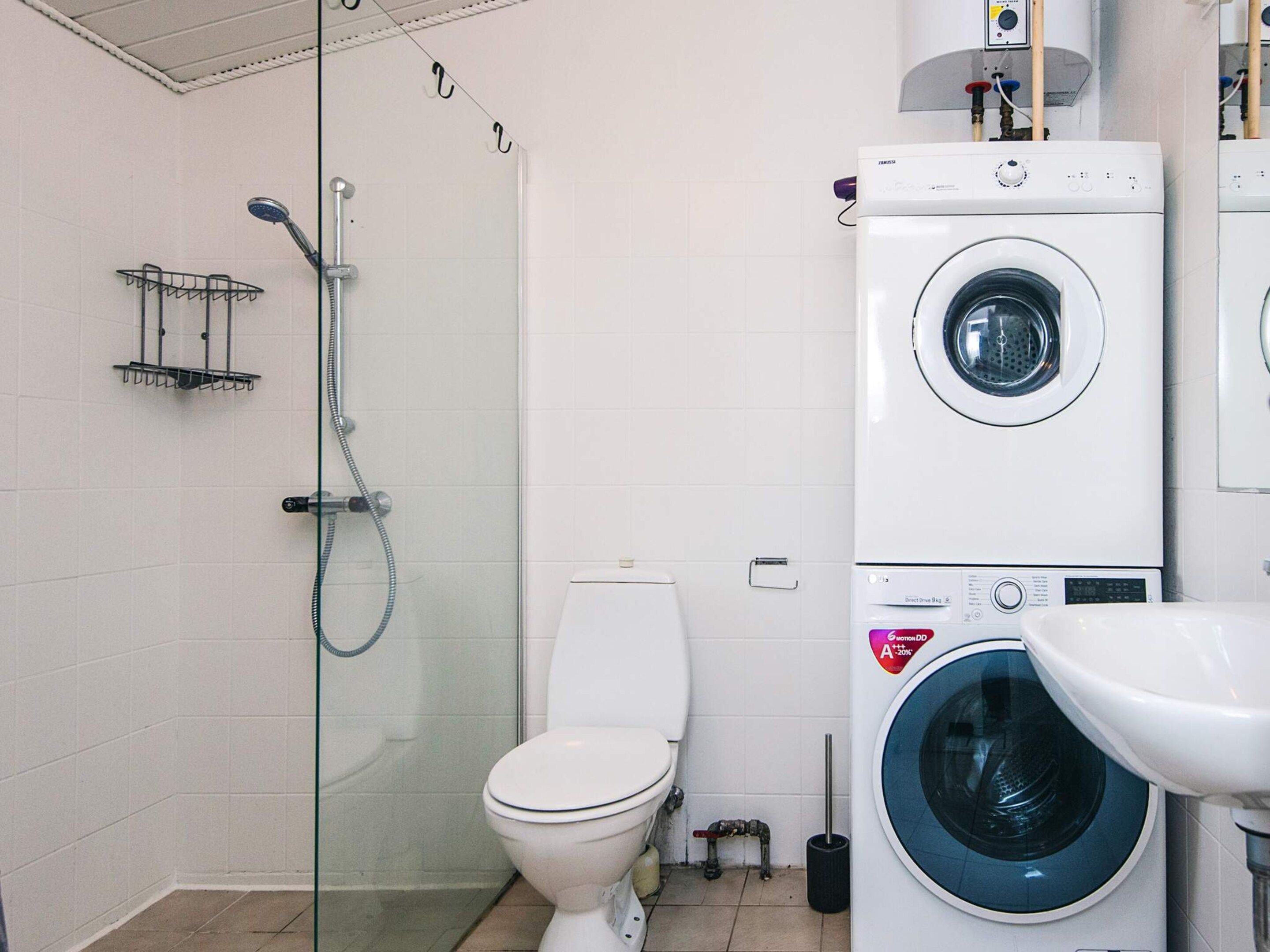 A bathroom with a glass-enclosed shower, a toilet, and two stacked washing machines.