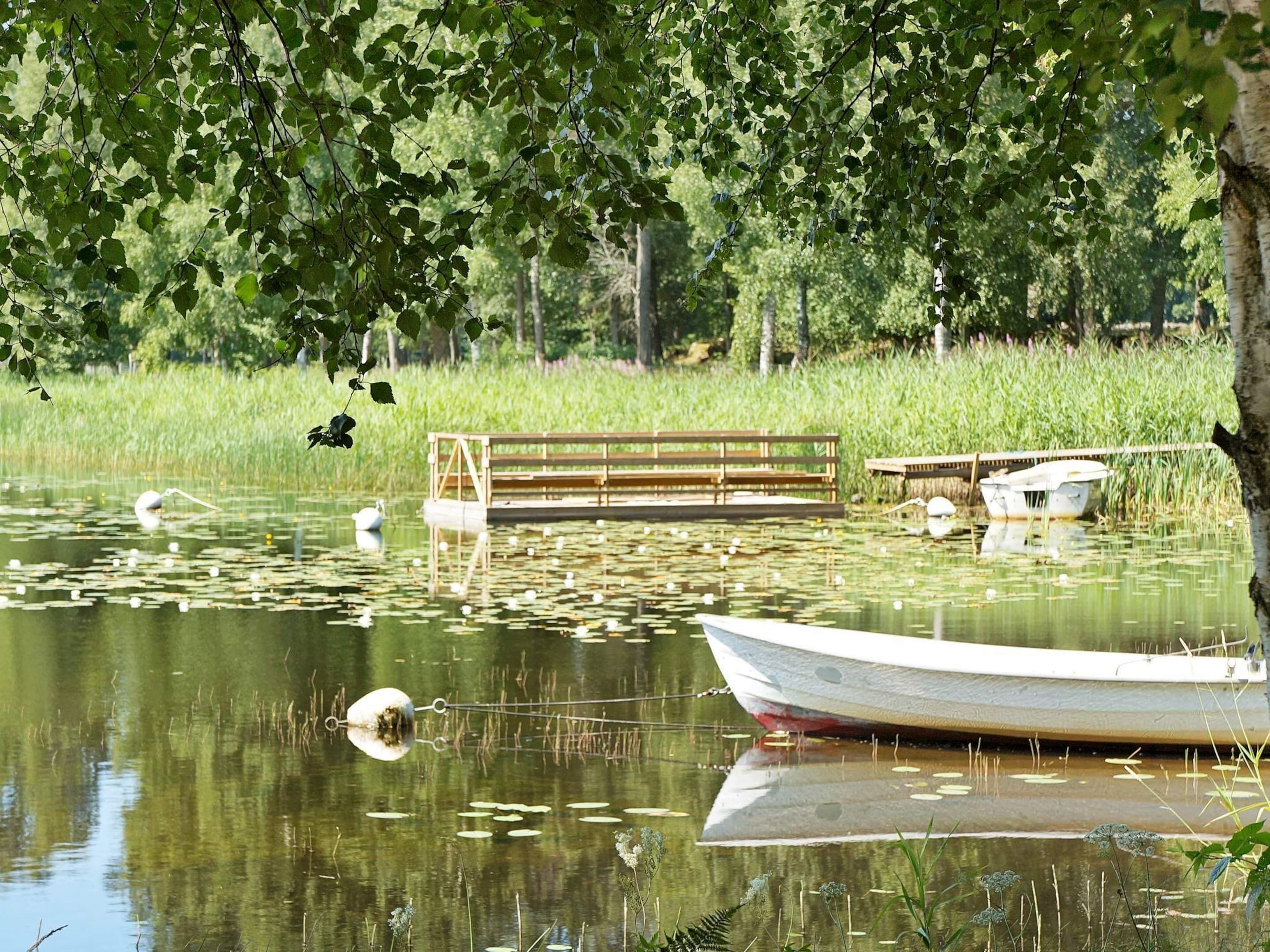 Un lago tranquilo con un muelle de madera, un banco y un bote pequeño.