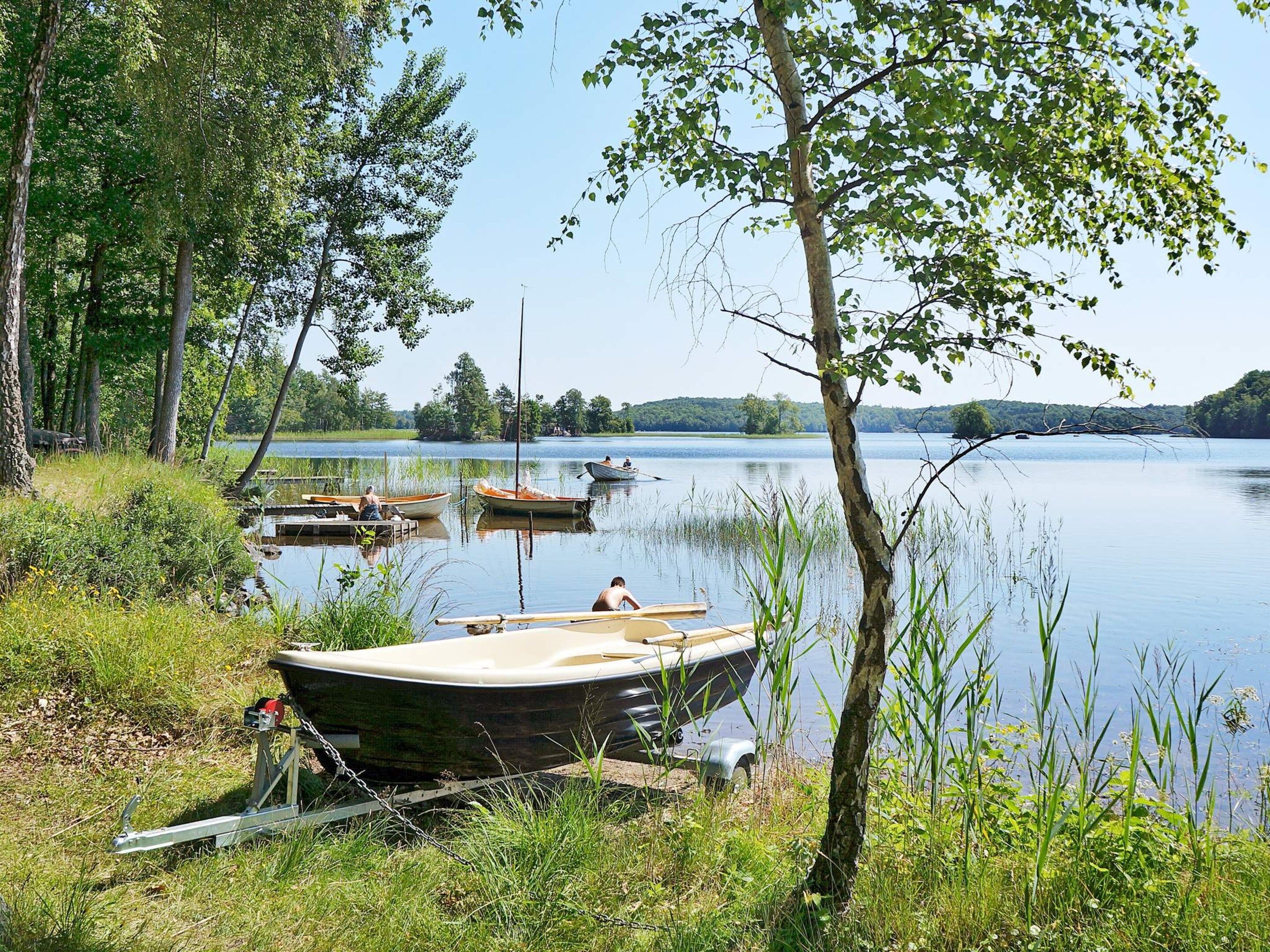 A calm lake with boats docked along the shore, surrounded by trees and grassy areas.