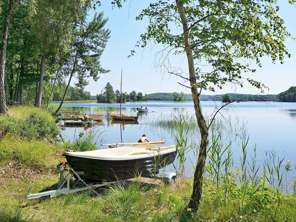 A calm lake with boats docked along the shore, surrounded by trees and grassy areas. - 4 Person Holiday Home in Hastveda (Hästveda)