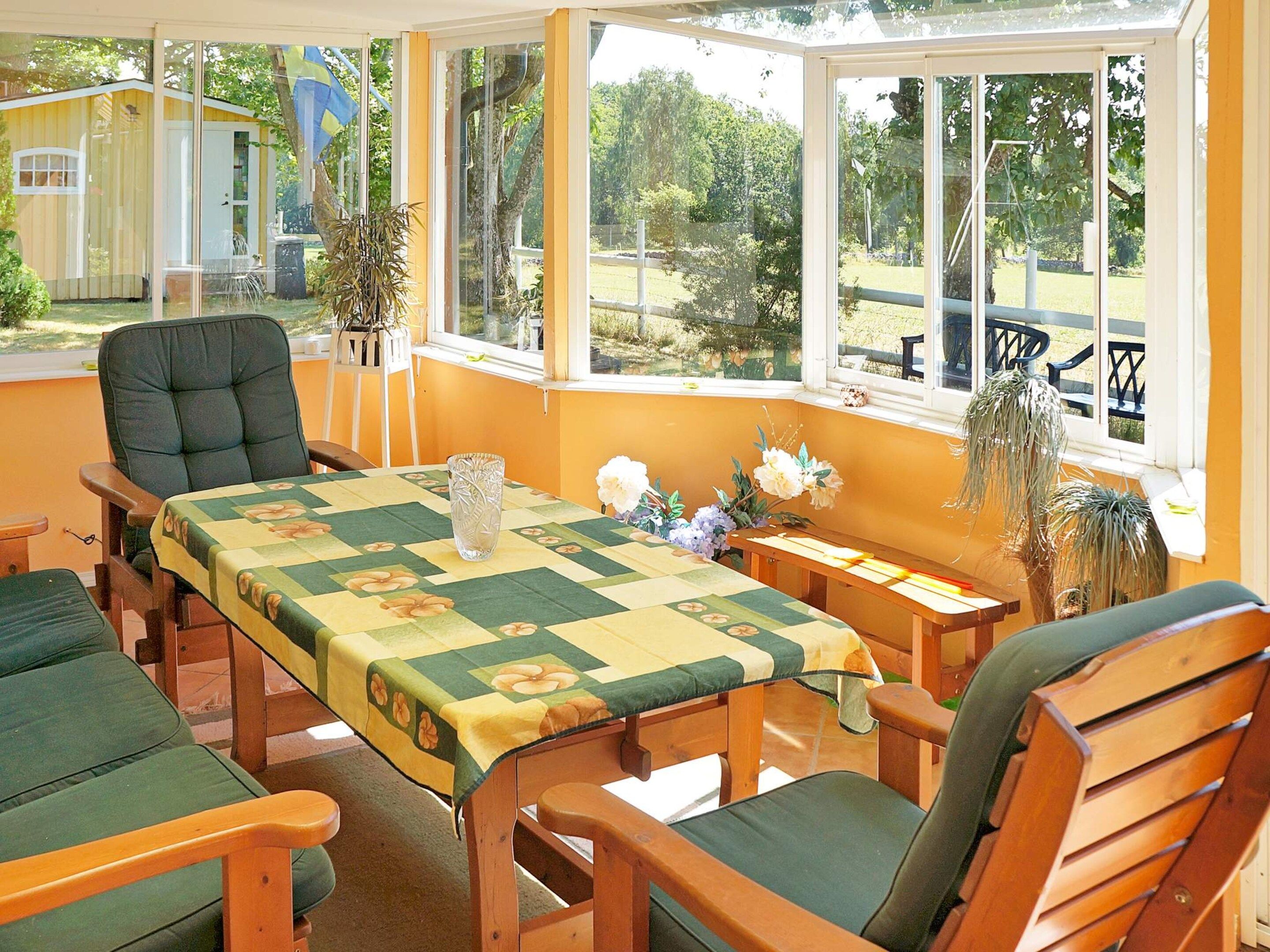 A sunroom with a table set for dining, surrounded by chairs, and large windows offering a view of the outdoors.