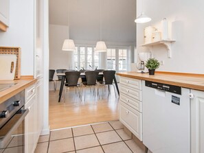 Eine moderne Küche mit Essbereich, weißen Schränken, einem Geschirrspüler und Pendelleuchten.