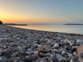 A pebbled beach with calm water and a clear sky.