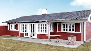 A red building with white trim, a tiled roof, and a small outdoor seating area with a table and stone planter. - 4 Star Holiday Home in Aabenraa (Aabenraa)