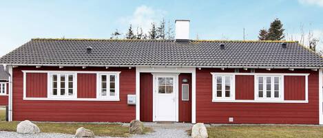 A red wooden building with a white door and windows, numbered 354, with a gravel driveway and rocks in front.
