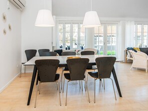 Ein moderner Essbereich mit einem langen Tisch, Stühlen, großen Fenstern und einer hängenden Leuchte.