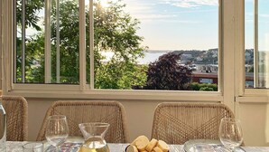 Una mesa de comedor dispuesta con mariscos, pan y copas de vino, con vistas a un paisaje que incluye agua y edificios.