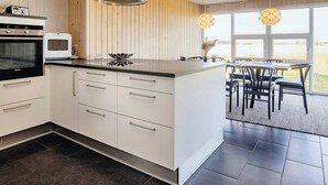 A modern kitchen with white cabinetry, a built-in oven, and a large island with a stainless steel range hood. - 4 Star Holiday Home in Hals (Hals)