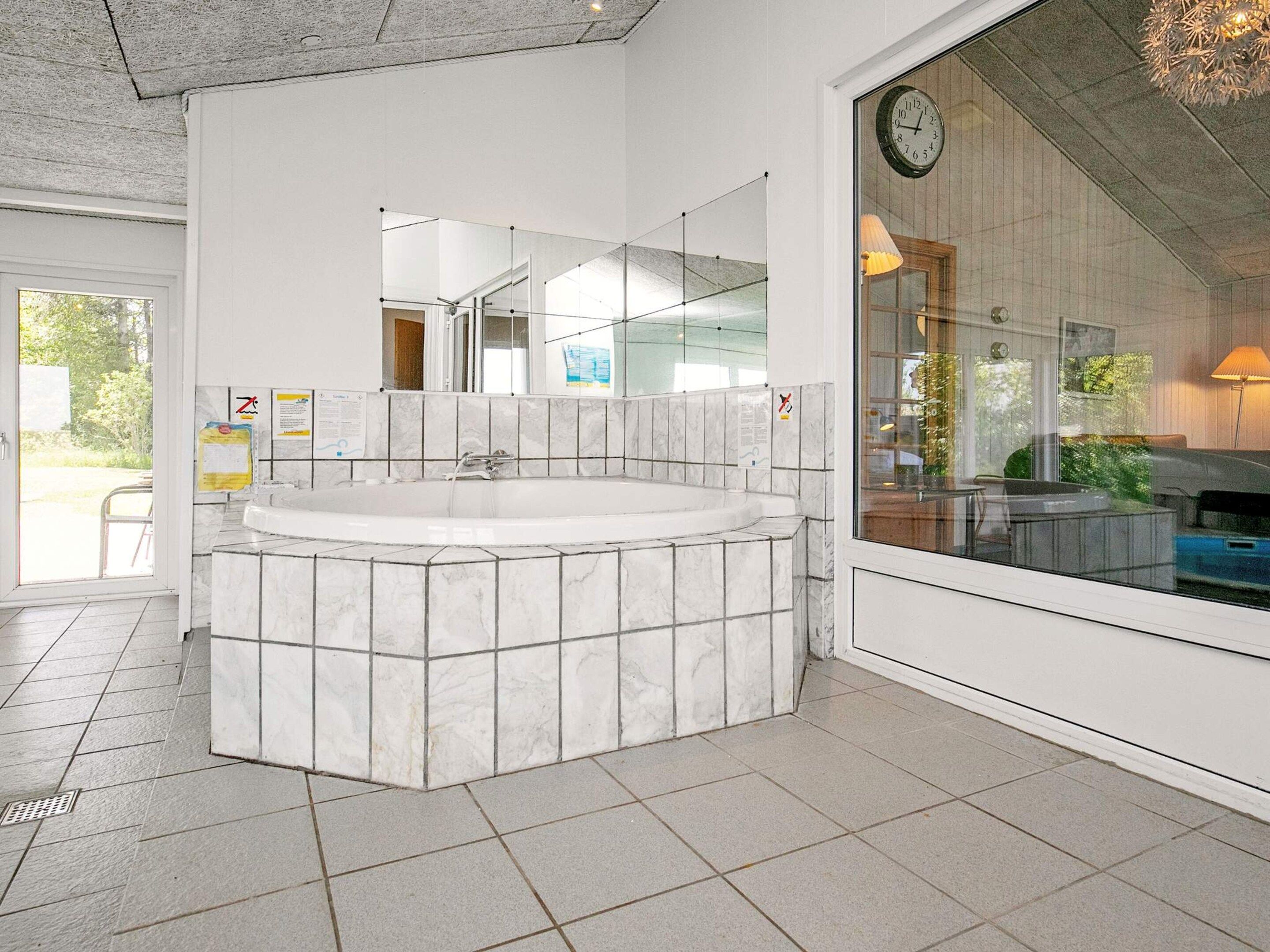 A modern bathroom with a freestanding bathtub, a large mirror, and a clock on the wall.