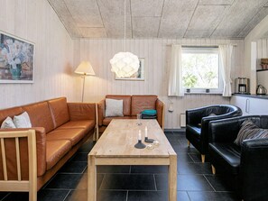 A living room with a wooden coffee table, two leather sofas, a floor lamp, and a window with curtains.