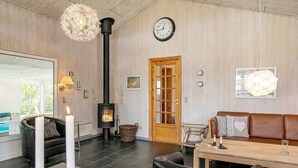 A cozy living room with a wood-burning stove, a leather sofa, a dining table, and a large window. - 4 Star Holiday Home in Hals (Hals)