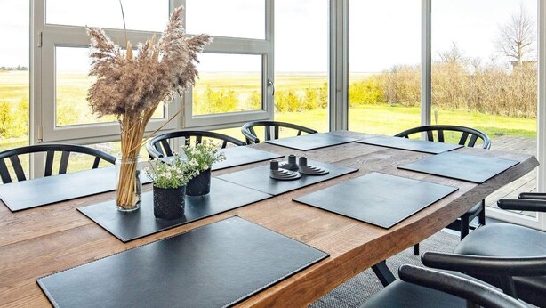 A dining area with a long wooden table, black chairs, and large windows offering a view of a field. - 4 Star Holiday Home in Hals (Hals)