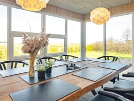 Un comedor con una larga mesa de madera, sillas negras y ventanas amplias que dan a un campo.
