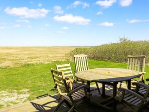 A wooden deck with a round table and four chairs, overlooking a grassy field.