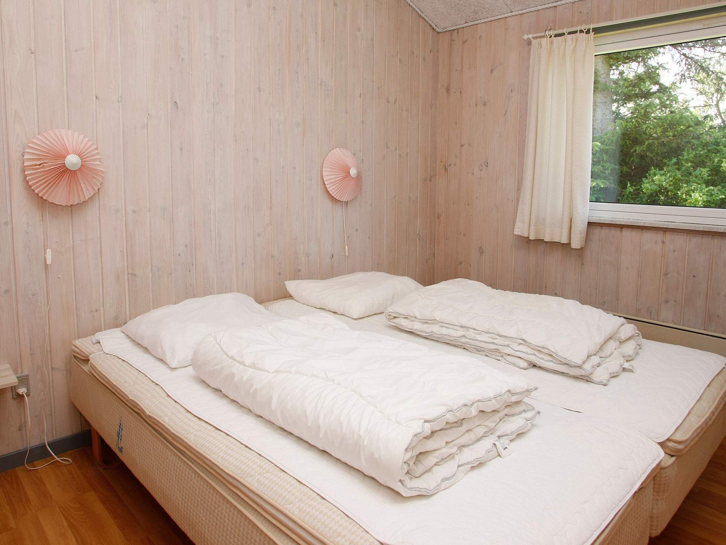 Ein Schlafzimmer mit zwei Betten, Holzwänden, einem Fenster mit Vorhang und zwei Wandventilatoren.