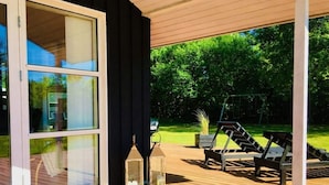 A covered outdoor area with a wooden deck, two lounge chairs, and a swing set. - 4 Star Holiday Home in Jerup (Jerup)