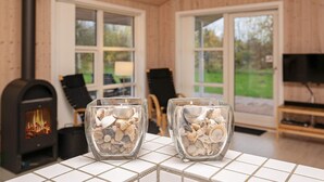 A cozy room with a wood-burning stove, two glass candle holders with seashells, and a television on a wooden stand. - 4 Star Holiday Home in Jerup (Jerup)
