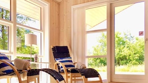 A sunlit room with wooden walls and large windows, featuring two lounge chairs with striped cushions and a table with a lamp. - 4 Star Holiday Home in Jerup (Jerup)