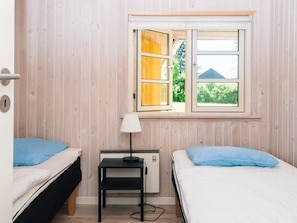 A room with two beds, a small table, a lamp, and a window with a view of greenery outside.