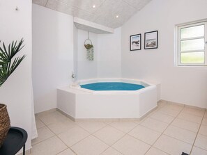 A modern bathroom with a freestanding bathtub, a hanging plant, and framed pictures on the wall.