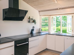 A modern kitchen with a black range hood, white cabinets, a built-in dishwasher, and a window with a view of greenery.