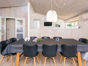 A modern dining area with a long table, black chairs, and a hanging light fixture.