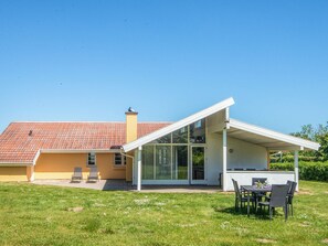 Moderni talo, jossa on patio, katettu ulkotila oleskelua varten ja kirkkaan sininen taivas.