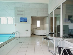 A swimming pool area with a glass partition, a white bathtub, and a table with chairs.