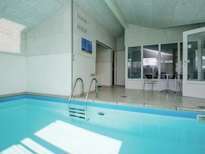 Una piscina coperta con acqua cristallina, scalette metalliche e pavimento piastrellato.